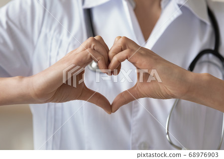 Close up young woman wearing uniform doctor showing heart gesture Close up young woman wearing uniform doctor showing heart gesture 68976903