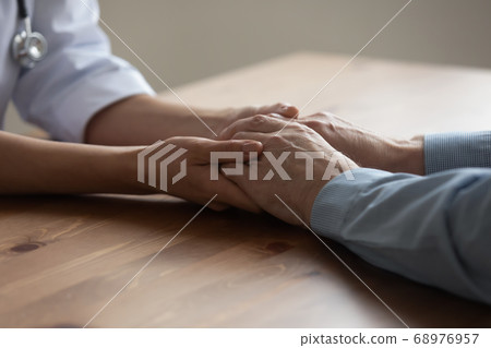 Close up caregiver comforting aged old patient, holding hands Close up caregiver comforting aged old patient, holding hands 68976957