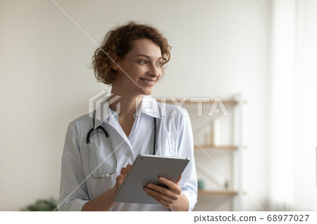 Close up smiling woman doctor holding digital tablet, pondering ideas 68977027