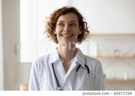 Head shot smiling dreamy young woman doctor standing in hospital 68977299