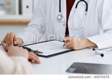Unknown woman-doctor filling up an application form while consulting patient. Medicine concept 68978379