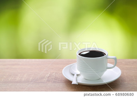 a cup of coffee and spoon on wood desk with beautiful green nature background a cup of coffee and spoon on wood desk with beautiful green nature background 68980680
