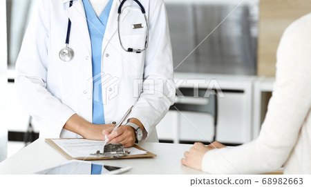 Unknown woman-doctor and patient in hospital. Blonde physician controls medication history records and exam results while using clipboard, close-up. Medicine concept Unknown woman-doctor and patient in hospital. Blonde physician controls medication history records and exam results while using clipboard, close-up. Medicine concept 68982663