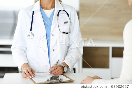 Unknown woman-doctor and patient in hospital. Blonde physician controls medication history records and exam results while using clipboard, close-up. Medicine concept Unknown woman-doctor and patient in hospital. Blonde physician controls medication history records and exam results while using clipboard, close-up. Medicine concept 68982667