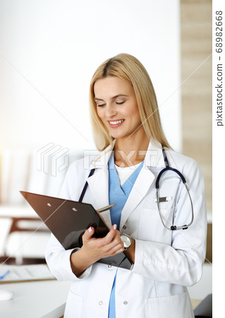 Doctor woman controls medication history records and exam results while using clipboard in sunny hospital . Medicine and healthcare concept Doctor woman controls medication history records and exam results while using clipboard in sunny hospital . Medicine and healthcare concept 68982668