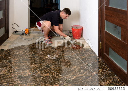 a man takes extra glue to install a ceramic brown 68982833