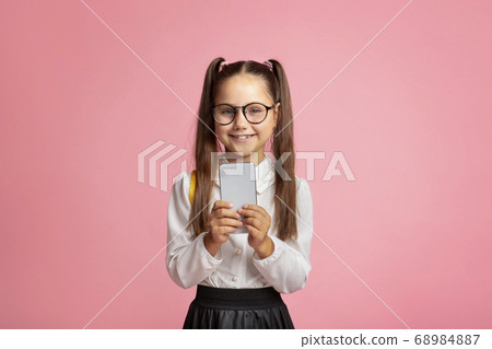 Modern technology and school. Smiling little girl with glasses holding smartphone 68984887