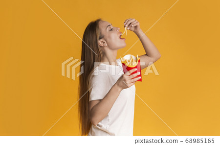 Hungry Millennial Girl Eating French Fries Serving, Standing Over Yellow Background 68985165