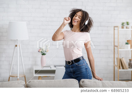 So much fun, stay home alone. African american girl has joy, singing at imaginary microphone and dancing with headphones 68985233