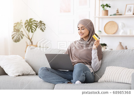 Cheerful Arabic Girl In Hijab With Laptop And Credit Making Online Shopping Cheerful Arabic Girl In Hijab With Laptop And Credit Making Online Shopping 68985368