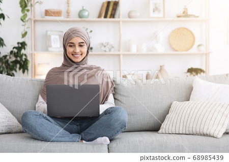 Online Education. Arabic Girl In Headscarf Using Laptop On Couch At Home Online Education. Arabic Girl In Headscarf Using Laptop On Couch At Home 68985439