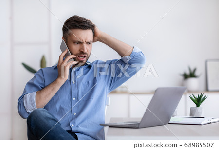 Frustrated businessman having problems with computer, talking on cellphone with customer support 68985507