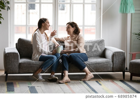 Young mixed race woman drinking coffee with 50s european mother. 68985874