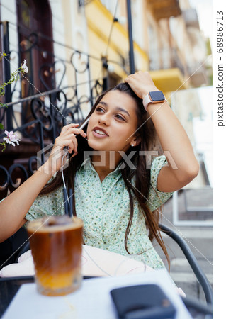 Attractive girl sitting outdoor street cafe, talking smartphone Attractive girl sitting outdoor street cafe, talking smartphone 68986713