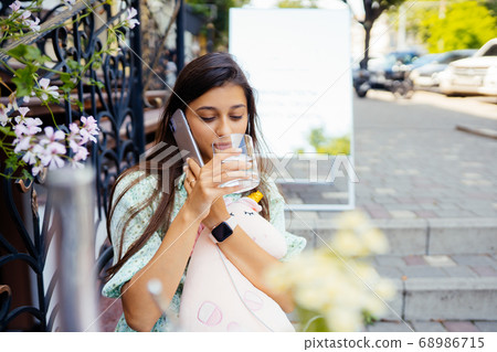Attractive girl sitting outdoor street cafe, talking smartphone Attractive girl sitting outdoor street cafe, talking smartphone 68986715