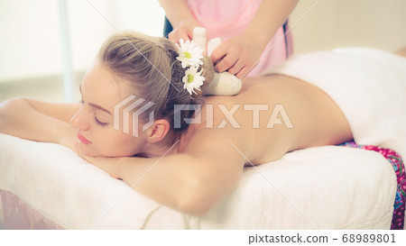 Massage therapist using herbal compress with woman 68989801