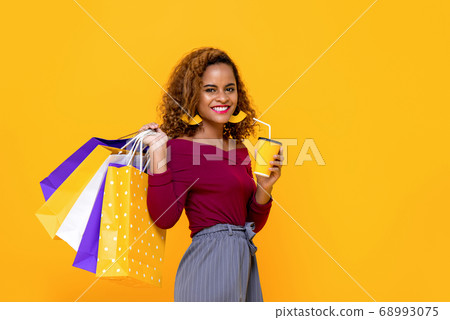 Cheerful African American woman with shopping bags and drink 68993075