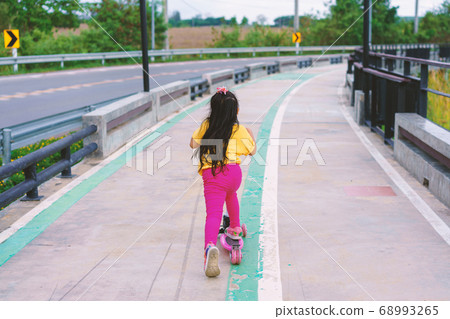 Little child girl to ride scooter in outdoor sports ground on sunny summer day. Active leisure  68993265