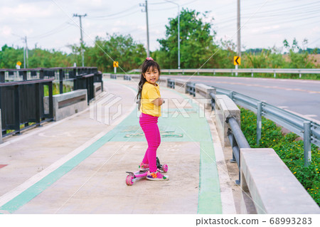 Little child girl to ride scooter in outdoor sports ground on sunny summer day 68993283