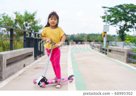 Little child girl to ride scooter in outdoor sports ground on sunny summer day 68993302
