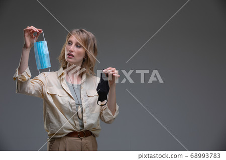 Head portrait attractive blond woman doing Difficult choice between surgical and tissue mask 68993783