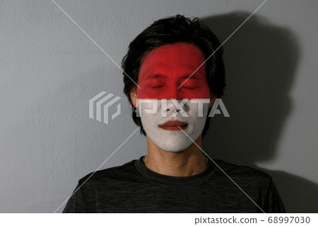 Portrait of a man with the flag of the Indonesia painted on his face and close eyes and black shadow 68997030