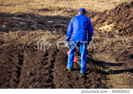 Worker with a machine cultivator digs the soil in 68998002