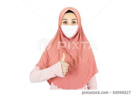 Great,Asian muslim woman with traditional dress wearing medical face mask make gesture thumps up isolated on white background 68998827