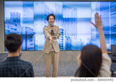A man taking a question on stage at a lecture 69000440