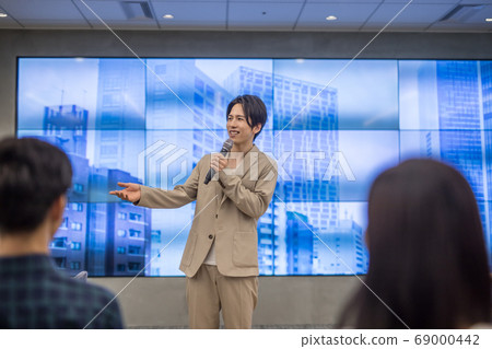 A man taking a question on stage at a lecture 69000442