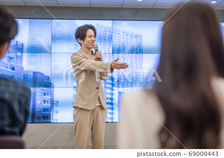 A man taking a question on stage at a lecture 69000443