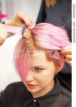 Hairdresser straights pink hair of woman by hair 69000891