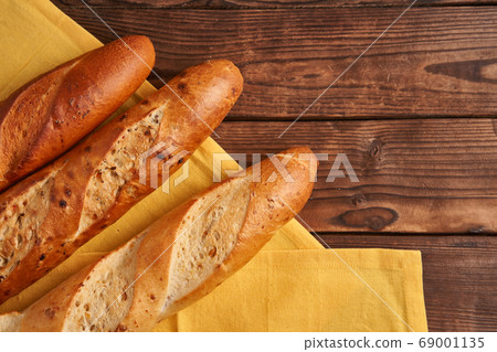 Three crispy french baguettes lie on an old wooden 69001135