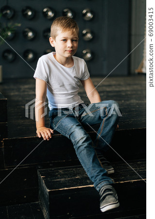 Portrait of handsome confident child boy sitting on dark floor posing in photo studio. 69003415