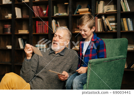Senior gray-haired grandfather with his grandson enjoy memories watching family photo album Senior gray-haired grandfather with his grandson enjoy memories watching family photo album 69003441