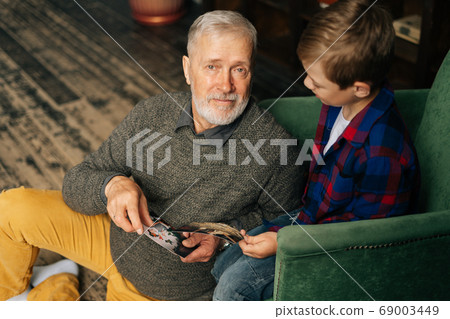 Top view of handsome gray-haired grandfather showing photo to his grandson, enjoy memories Top view of handsome gray-haired grandfather showing photo to his grandson, enjoy memories 69003449