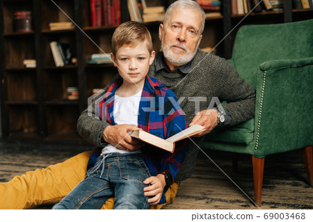 Portrait of child boy sitting with his grandfather and reading an interesting book 69003468