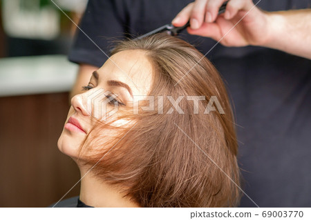 Hand of hairdresser combs hair of young woman Hand of hairdresser combs hair of young woman 69003770