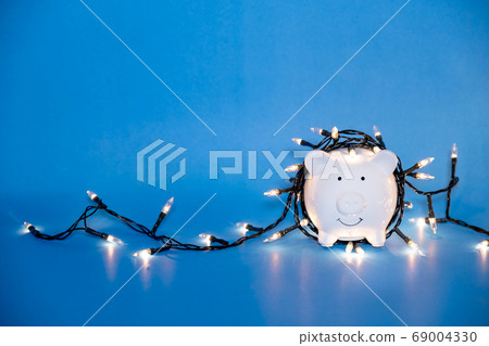 White piggy bank with Christmas string lights on happy December festival White piggy bank with Christmas string lights on happy December festival 69004330