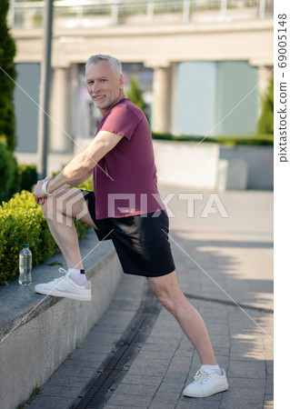 Mature grey-haired male stretching his knee outside Mature grey-haired male stretching his knee outside 69005148