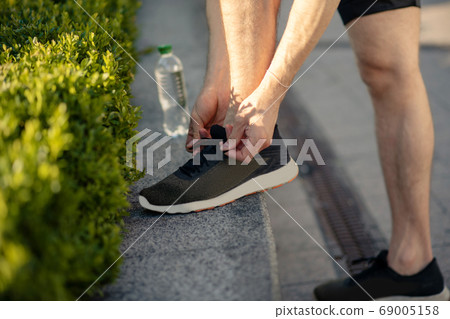 Close-up of male hands lacing up black sneakers Close-up of male hands lacing up black sneakers 69005158