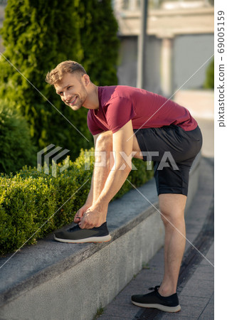 Young bearded male lacing up his sneakers, smiling Young bearded male lacing up his sneakers, smiling 69005159