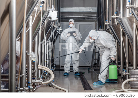 Product quality and disinfection. Men in hazmat suits work with spray bags in beer factory Product quality and disinfection. Men in hazmat suits work with spray bags in beer factory 69006180