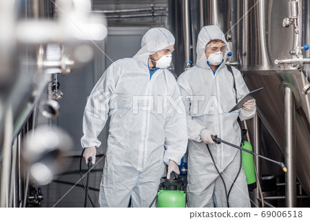 Quality control equipment. Men in protective suits and masks look at tablet Quality control equipment. Men in protective suits and masks look at tablet 69006518
