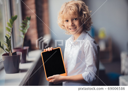 Cute blonde boy showing his tablet and smiling Cute blonde boy showing his tablet and smiling 69006586