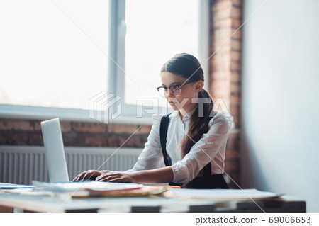 Cute brunette girl in eyeglasses typing and looking serious Cute brunette girl in eyeglasses typing and looking serious 69006653