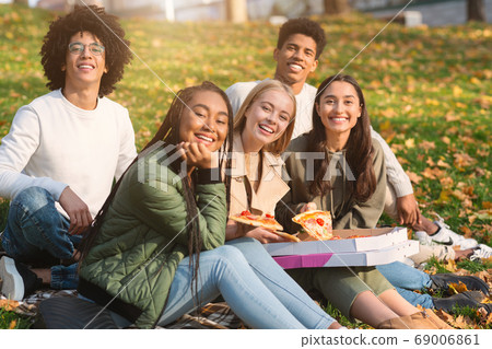 Happy teenagers smiling at camera while grabbing pizza from box Happy teenagers smiling at camera while grabbing pizza from box 69006861