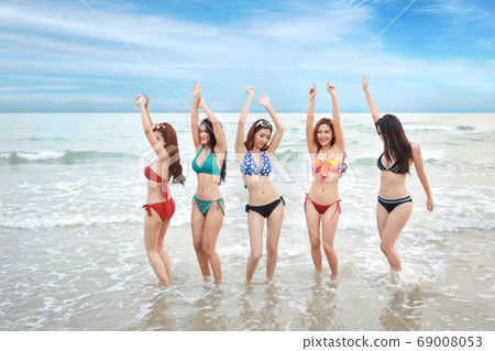 young asian beautiful and joyful girls in bikini dancing and raising hands on tropical beach   69008053