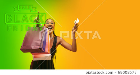 Portrait of young woman in neon light on gradient backgound. The human emotions, black friday, cyber monday, purchases, sales, finance concept. Neoned lettering. Portrait of young woman in neon light on gradient backgound. The human emotions, black friday, cyber monday, purchases, sales, finance concept. Neoned lettering. 69008575