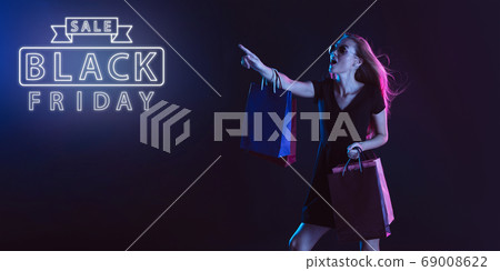 Portrait of young woman in neon light on dark backgound. The human emotions, black friday, cyber monday, purchases, sales, finance concept. Neoned lettering. 69008622